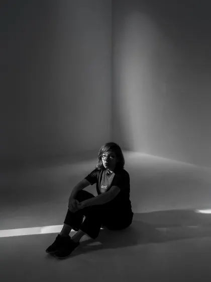 A moody black and white portrait of me, sitting in a corner with a single beam of light. It reflects the contemplative and artistic side of my work.