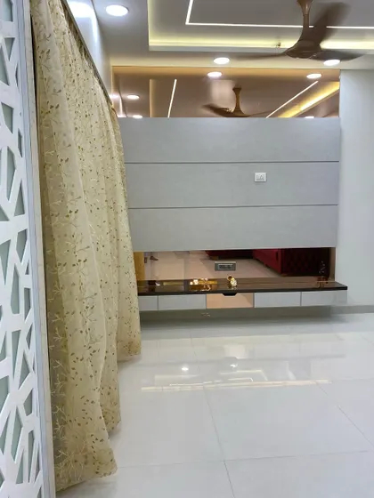 This living room features a floating TV console with a mirrored base, which creates an illusion of more space. The design is complemented by a decorative jaali partition and elegant curtains.