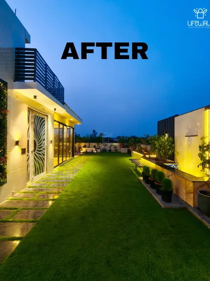 A beautiful "after" shot of a complete terrace makeover. The space now includes a lush lawn, a water feature, and a glass-enclosed room, all illuminated for a stunning evening view.