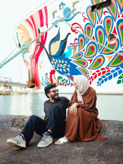 The couple sits by the water, sharing a laugh against the backdrop of a brightly painted ship. A perfect blend of romance and fun.