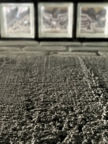 A macro shot focusing on the rough texture of a concrete wall, with glass blocks providing a smooth, translucent contrast in the background. It’s a study in how different material surfaces interact with light.