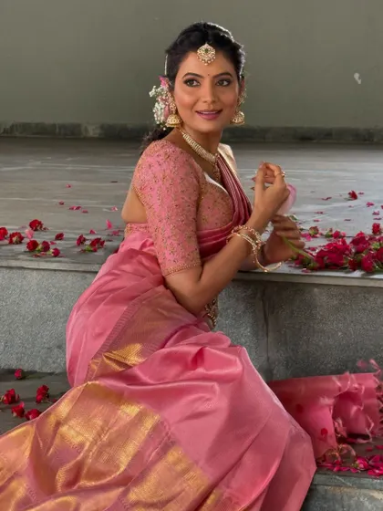 Shwetha Prasad seated amidst rose petals, looking lovely in the custom pink Kanchivaram saree and embroidered blouse.