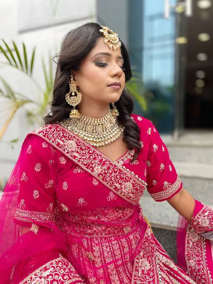 A beautiful bridal look in a vibrant pink lehenga. The soft curls, kundan jewellery, and flawless makeup are a testament to the skills our students develop.