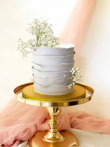 A minimalist cake with a unique grey ruffled buttercream texture. It's simply adorned with sprigs of fresh baby's breath for an ethereal look.