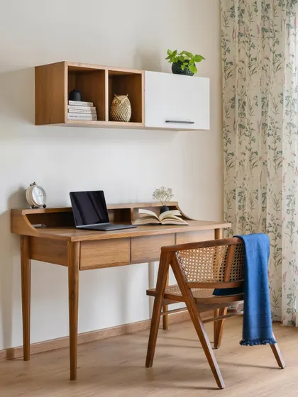 A modern Indian vibe defines this study nook in the 'House of Kismish' project. The space features a sleek wooden desk with elegant tapered legs and a floating overhead storage unit.
