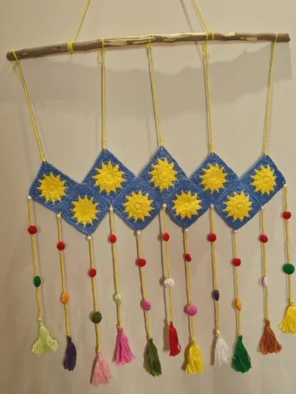 A closer look at the sun-themed crochet wall decor. This piece is hung on a natural wood branch and features colorful tassels and beads.
