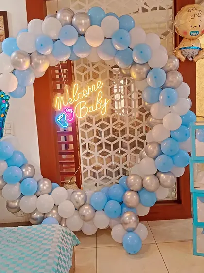 A "Welcome Baby" decoration for a boy, featuring a blue, white, and silver balloon ring, a neon sign, and 'BABY' blocks.