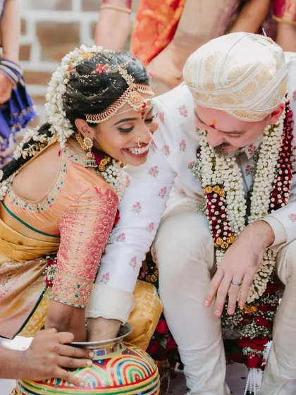 A joyful moment from a South Indian wedding ritual, with the couple laughing as they participate in a traditional game, showcasing candid happiness.