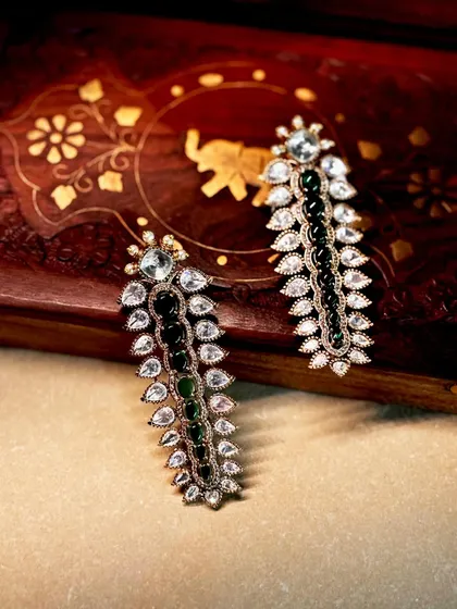 Bespoke earrings designed to be remembered. This pair features a long, leaf-like design with alternating lines of polki diamonds and green stones.
