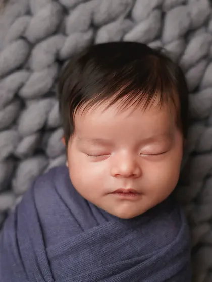 A close-up on the face of the newborn in the blue wrap, highlighting his peaceful expression and beautiful dark hair.