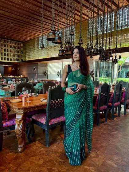 A solo shot of my Teej brunch look. The emerald green leheriya saree is paired with a simple black sleeveless blouse, which makes the traditional print feel modern and chic. The look is completed with a matching green clutch.