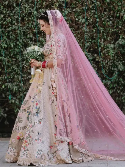 A full-length side profile of the bride, her long pink veil creating a dramatic and beautiful trail behind her.