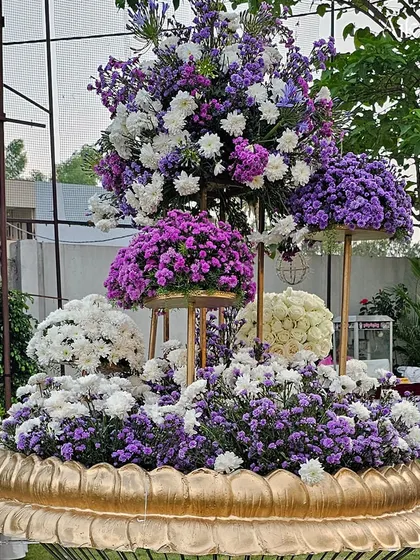 A magnificent floral centerpiece featuring tiers of purple and white flowers arranged in a golden lotus-shaped base. This is a perfect example of opulent floral art.