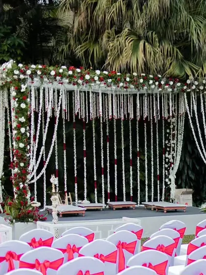 A beautiful mandap setup for an outdoor ceremony, framed with white and red flowers and delicate hanging floral strings for a classic and romantic feel.