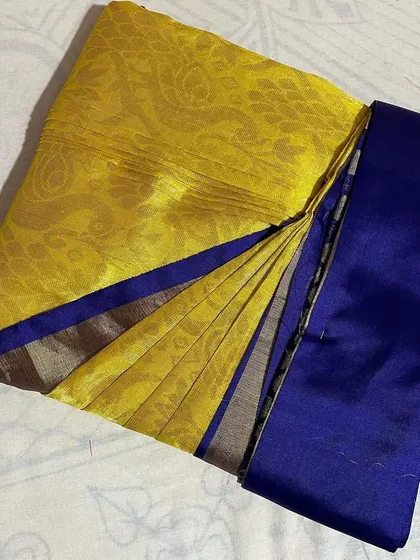 This yellow and blue silk saree is perfectly pleated, showing off its contrasting border. It's now ready for the customer to wear.