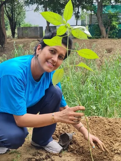 A volunteer from NTT DATA smiles as she plants a native Chamrod sapling, a species that helps bind fragile soil and provides food for bees and birds.