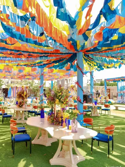 Colorful guest seating under a canopy of blue, yellow, and orange fabric strips. The unique tables and bold blue and orange chairs continue the vibrant, art-inspired theme.
