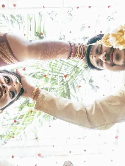 A unique low-angle shot looking up at the couple during a Telugu wedding ritual. Their happy, smiling faces are framed against the sky, creating a joyful and unconventional wedding portrait.