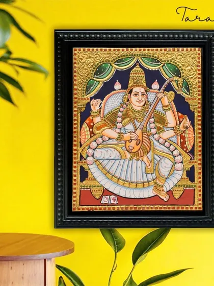A radiant Tanjore painting of Goddess Saraswati, the patron of knowledge, music, and the arts. Her serene presence is beautifully captured with delicate gold details and a pristine white saree.