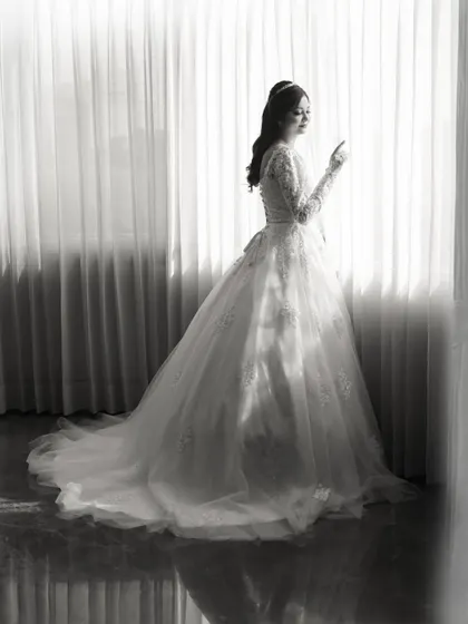 A classic black and white portrait of the bride in her beautiful white gown, looking out the window.