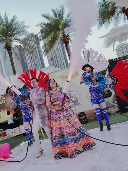 The couple makes a grand entrance at their carnival with CO2 guns, surrounded by performers in vibrant costumes. It's all about creating high-energy, memorable moments.