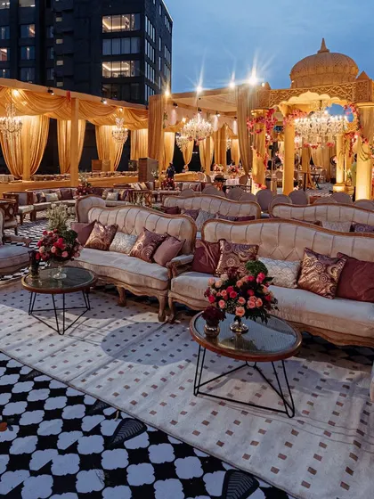 The lounge seating area, with plush vintage-style sofas and floral centerpieces. The checkered floor provides a bold contrast to the golden drapes and structures.