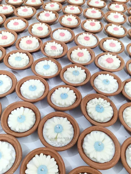 A closer look at the white and blue daisy clay pot candles, highlighting the delicate, handmade flower details.