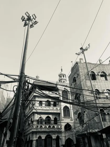 The contrast of old Mughal-style architecture with modern streetlights and electrical wires.