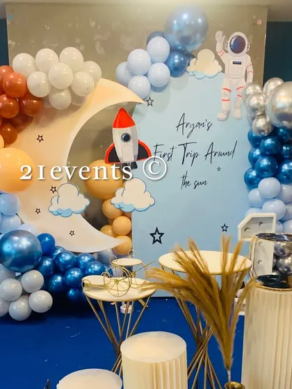 A 'First Trip Around the Sun' astronaut theme. This setup features a moon cutout, a rocket, and a beautiful balloon galaxy in shades of blue, orange, and chrome.