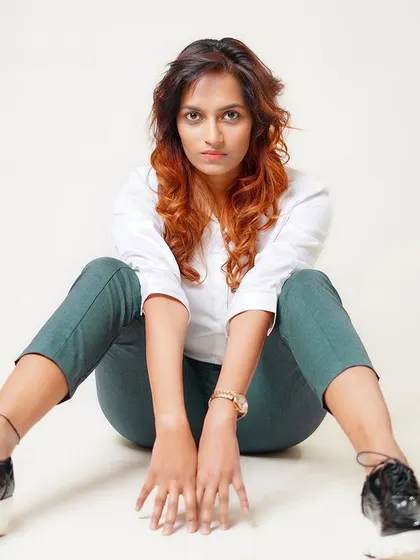 A modern, powerful seated pose on the studio floor. The combination of a classic white shirt with casual trousers and platform shoes creates a contemporary look.
