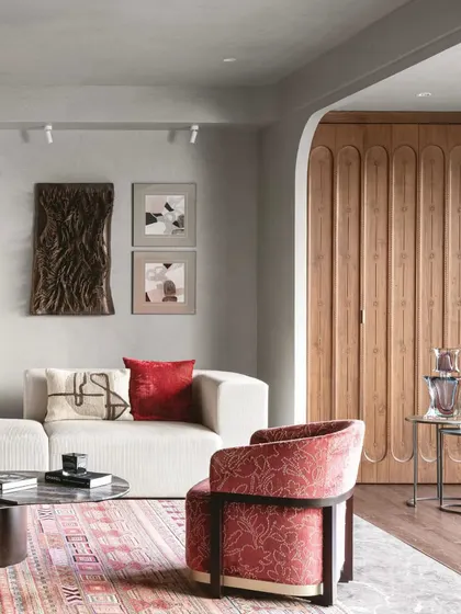 Here, you can see how we use custom woodwork to add warmth and character. The fluted wooden panel conceals a door, creating a seamless and elegant wall feature. The pops of red in the armchair and cushions add a touch of vibrancy to the calm, neutral palette.