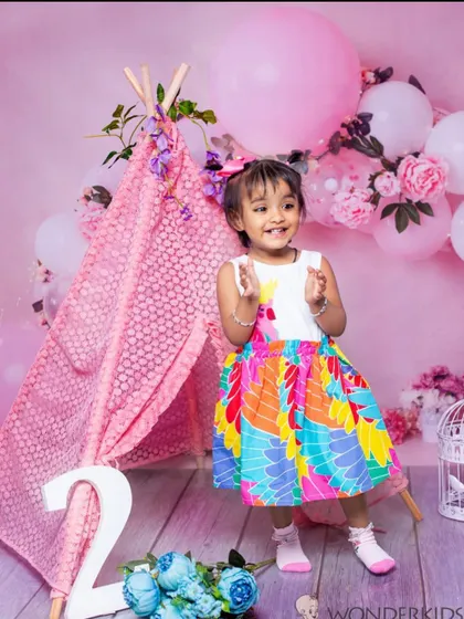 A joyful toddler claps her hands with excitement during her second birthday photoshoot. The colorful dress and pink teepee setup make this a vibrant and happy celebration.
