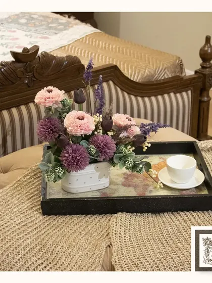 Bringing timeless beauty into your home, one bloom at a time. This lovely arrangement of pink and purple flowers is styled on a decorative tray, perfect for a bedside table or ottoman.