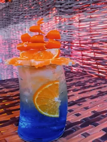 A fun and creative mocktail, perfect for a themed party. This blue and orange drink is garnished with intricately carved carrots and oranges to look like a pirate ship.