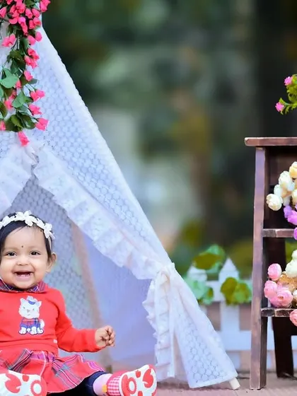 A happy baby girl in a red outfit playing in a floral teepee setup.