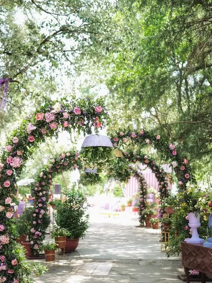 A beautiful garden pathway lined with multiple arches of pink roses, creating a romantic walkway.
