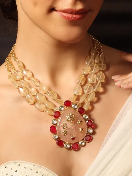 A vibrant necklace with a large pink stone pendant surrounded by rubies, strung on multiple strands of yellow beads.