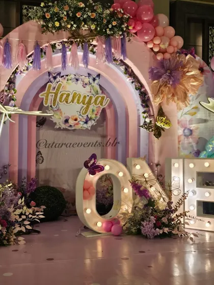 The main stage for Hanya's first birthday, featuring a rainbow arch, 'ONE' marquee lights, and an abundance of flowers and balloons, all in a dreamy butterfly theme.