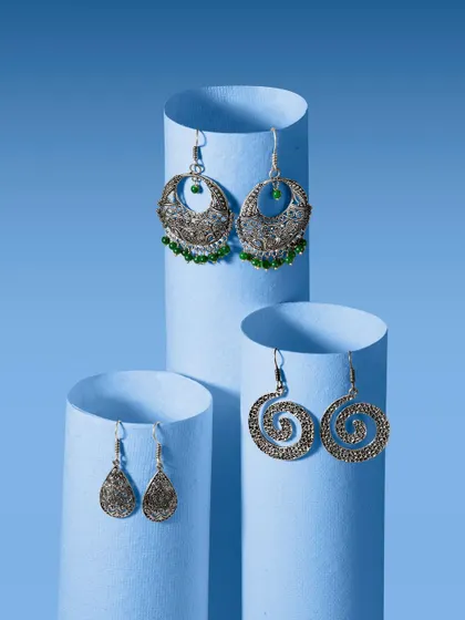A creative studio shot of three pairs of oxidized silver earrings, displayed on blue paper cylinders. This simple yet effective setup isolates each product while creating a cohesive and artistic group photo.