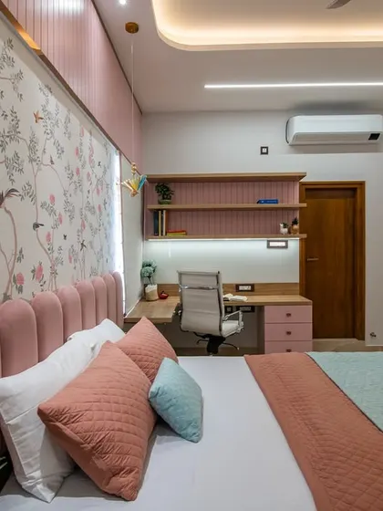 The study area in the daughter's bedroom, featuring a pink desk with open shelving and a comfortable white office chair. The floral wallpaper and soft color palette create an inspiring and pleasant workspace.