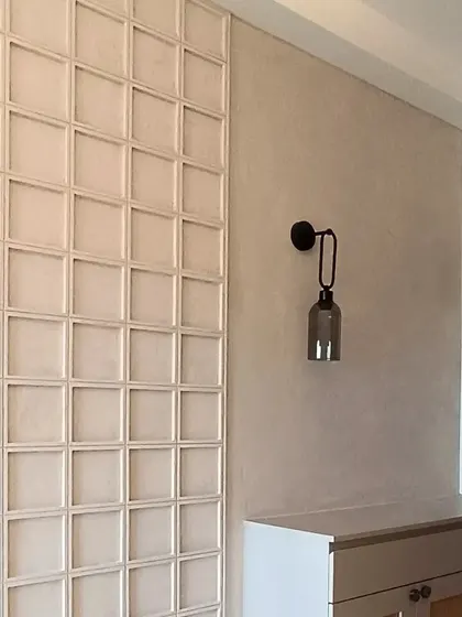A bohemian-inspired foyer unit with a textured wall panel featuring square woodwork. The design is complemented by a sleek black wall sconce, mixing earthy textures with modern accents.