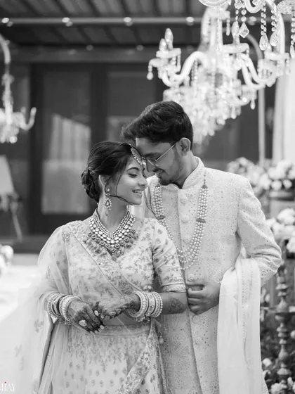 A timeless black and white photo of the couple sharing a gentle moment under a grand chandelier.