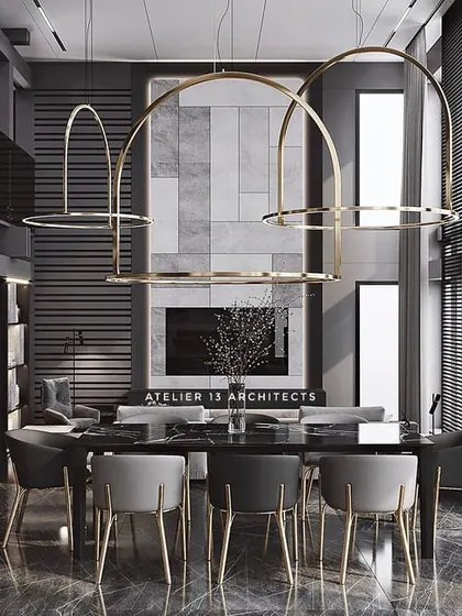 A dining room with a bold, monochromatic design. Large, arched brass chandeliers hang over a black dining table, while grey and black chairs with brass legs continue the theme. The double-height space feels grand and contemporary.