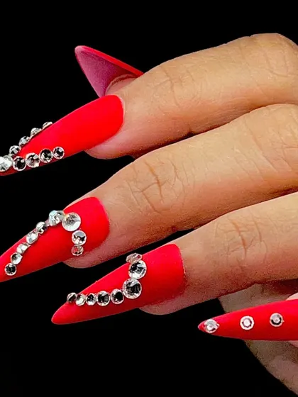A bold and glamorous look for any celebration, featuring long, stiletto nails in matte red, adorned with sparkling rhinestones.