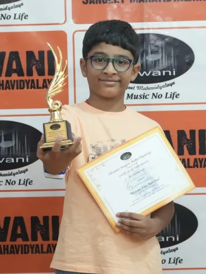A young student proudly holds up his certificate and trophy.