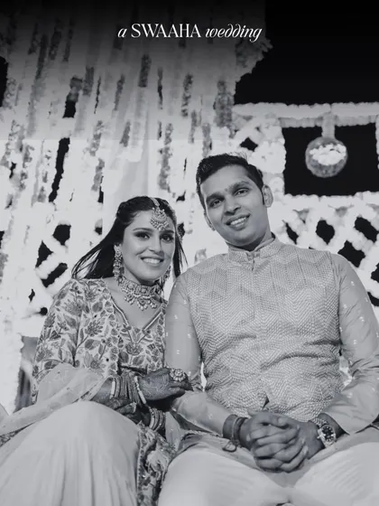 A classic black and white portrait of a couple at their Haldi ceremony, seated against a backdrop of hanging florals.