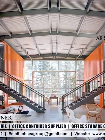 The interior of this multi-level container home reveals a spacious, open-plan design with a double-height ceiling and dramatic staircases. The original orange container walls are left exposed for an industrial-luxe feel.