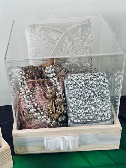A beautiful gift for a baby shower, packed in a pinewood box with an acrylic lid. It includes a traditional outfit, a potli bag, and a jeweled clutch.