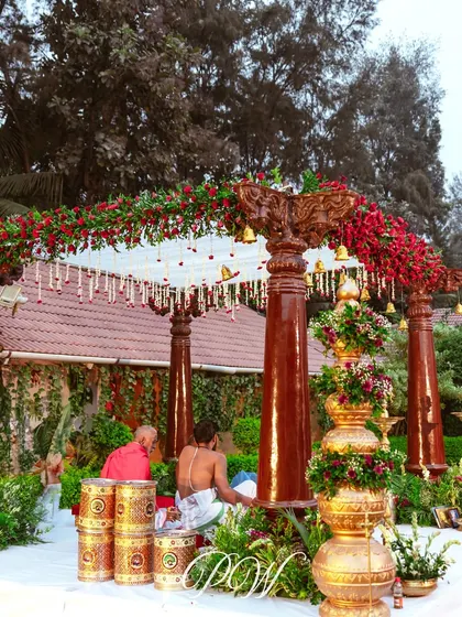 A classic South Indian wedding mandap with polished wooden pillars, a canopy of red roses, and traditional brass lamps. This setup is perfect for an intimate and authentic Muhurtham.