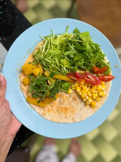 A deconstructed vegetarian wrap showing all the fresh ingredients: corn, cherry tomatoes, bell peppers, and a mix of lettuce and arugula on a whole grain tortilla.
